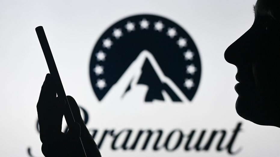 Paramount global logo in background with a woman holding up phone in front