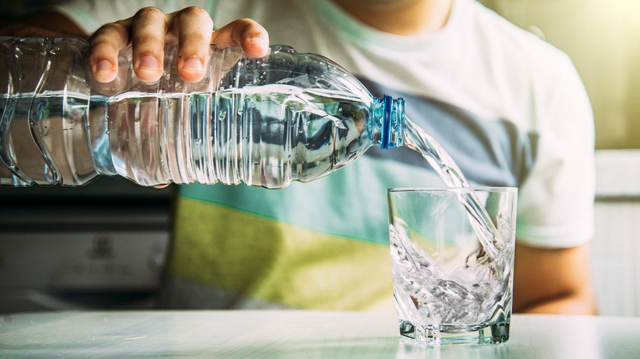 A person pouring bottled water into a glass